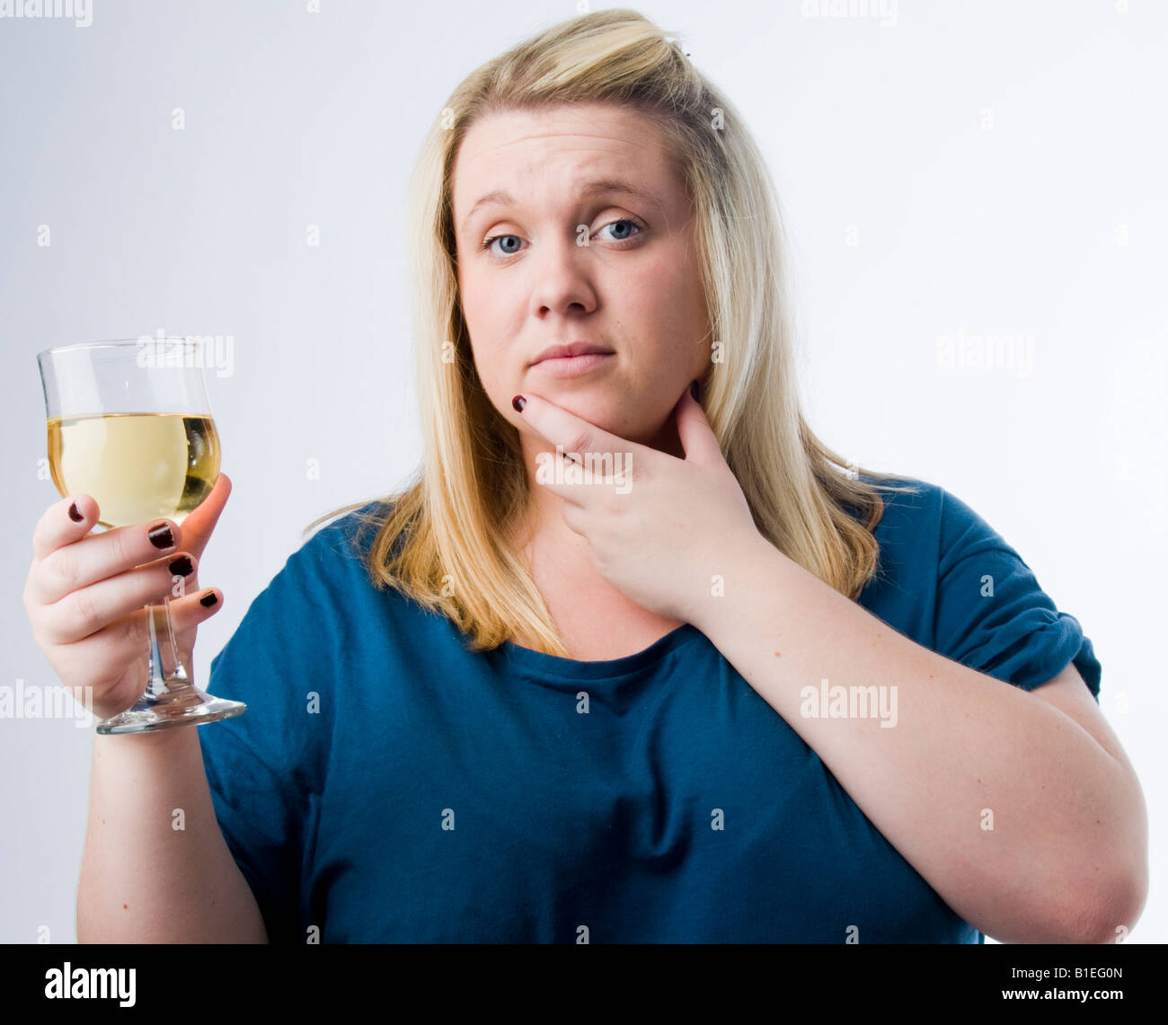 An overweight blonde young woman drinking a glass of white wine looking