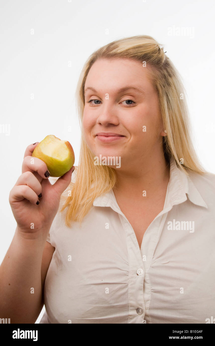 young overweight fat woman girl on a diet eating an apple; blonde hair, white background in studio Stock Photo