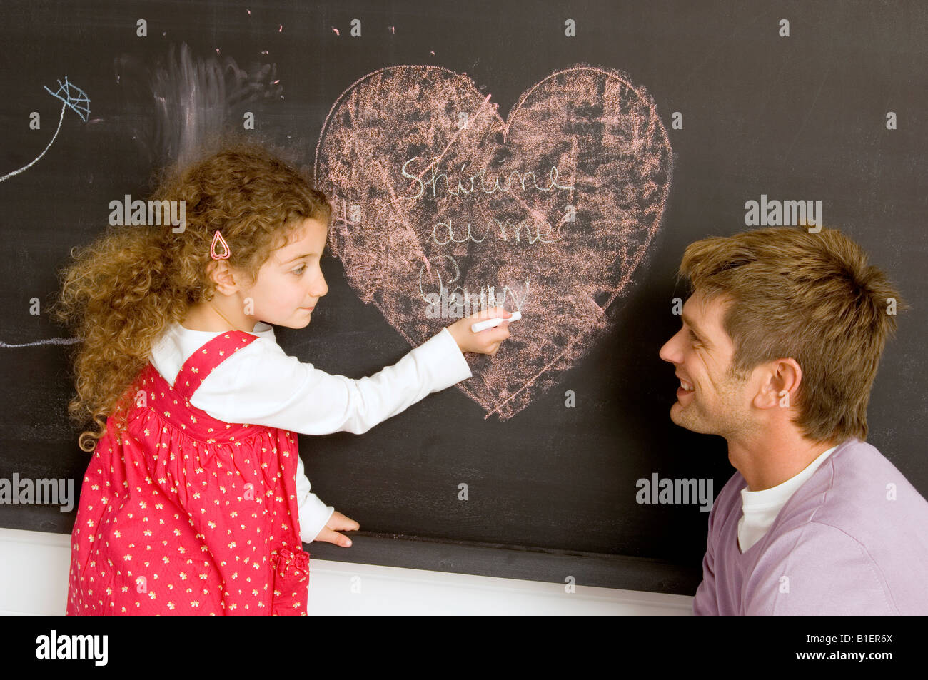 side profile of a girl drawing on the blackboard with her father