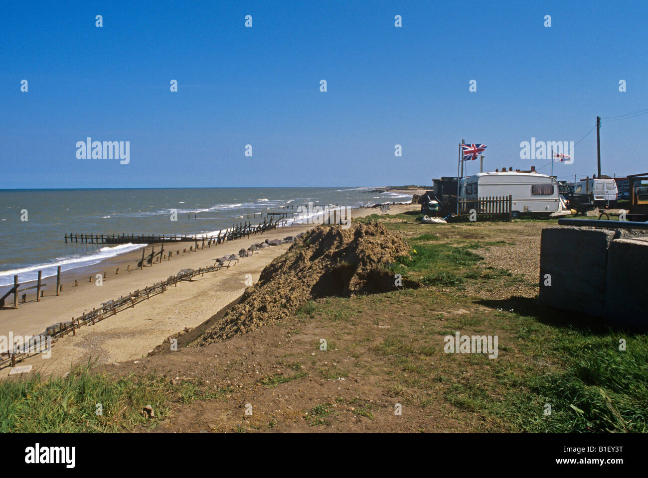 battered sea defences and flying flags on caravans at Happisburgh Stock Photo