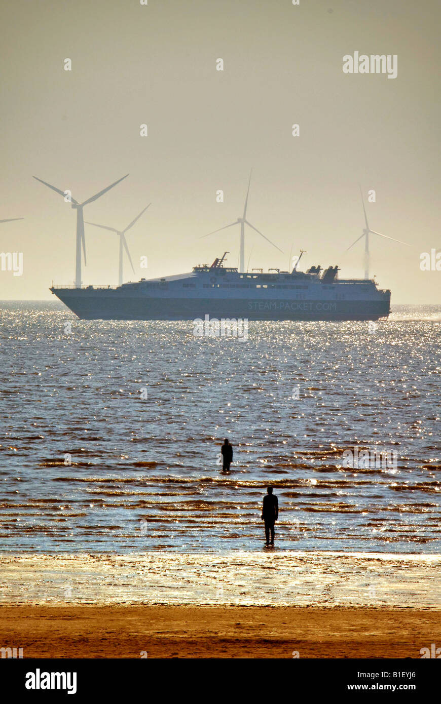 Antony Gormley statues on Crosby beach. Windmills  for electricity in the river Mersey and Isle of Man ferry. Stock Photo