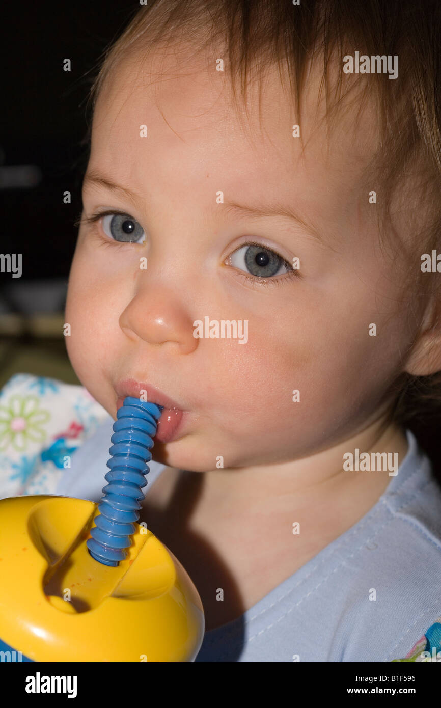 15 month old toddler drinking from a plastic cup with a straw Stock Photo