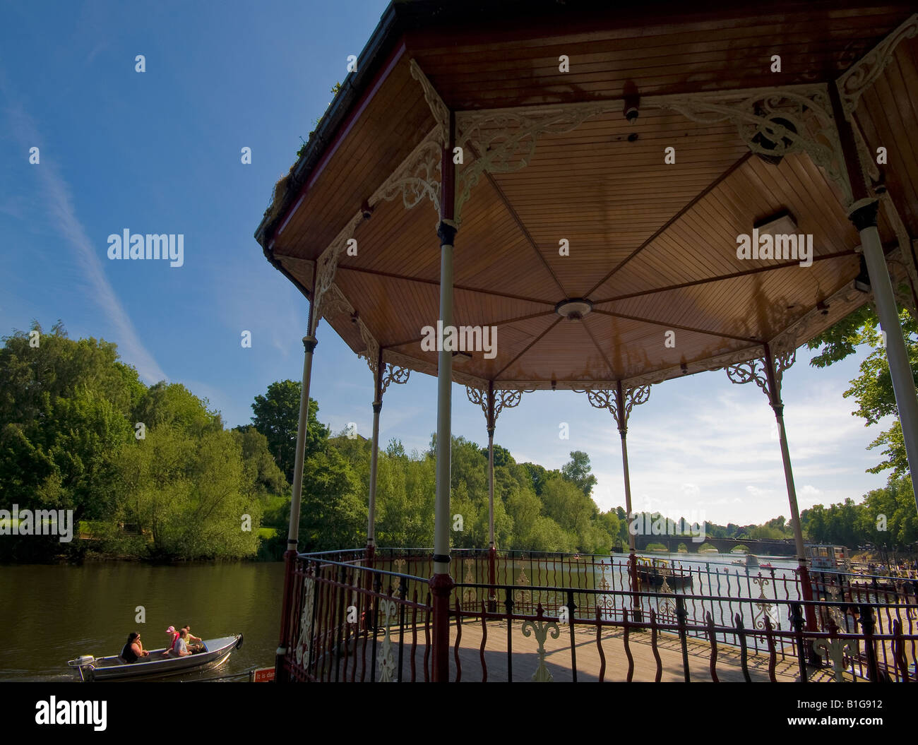 Holiday makers in a small motor launch pass a traditional bandstand on the banks of the River Dee in Chester UK Stock Photo