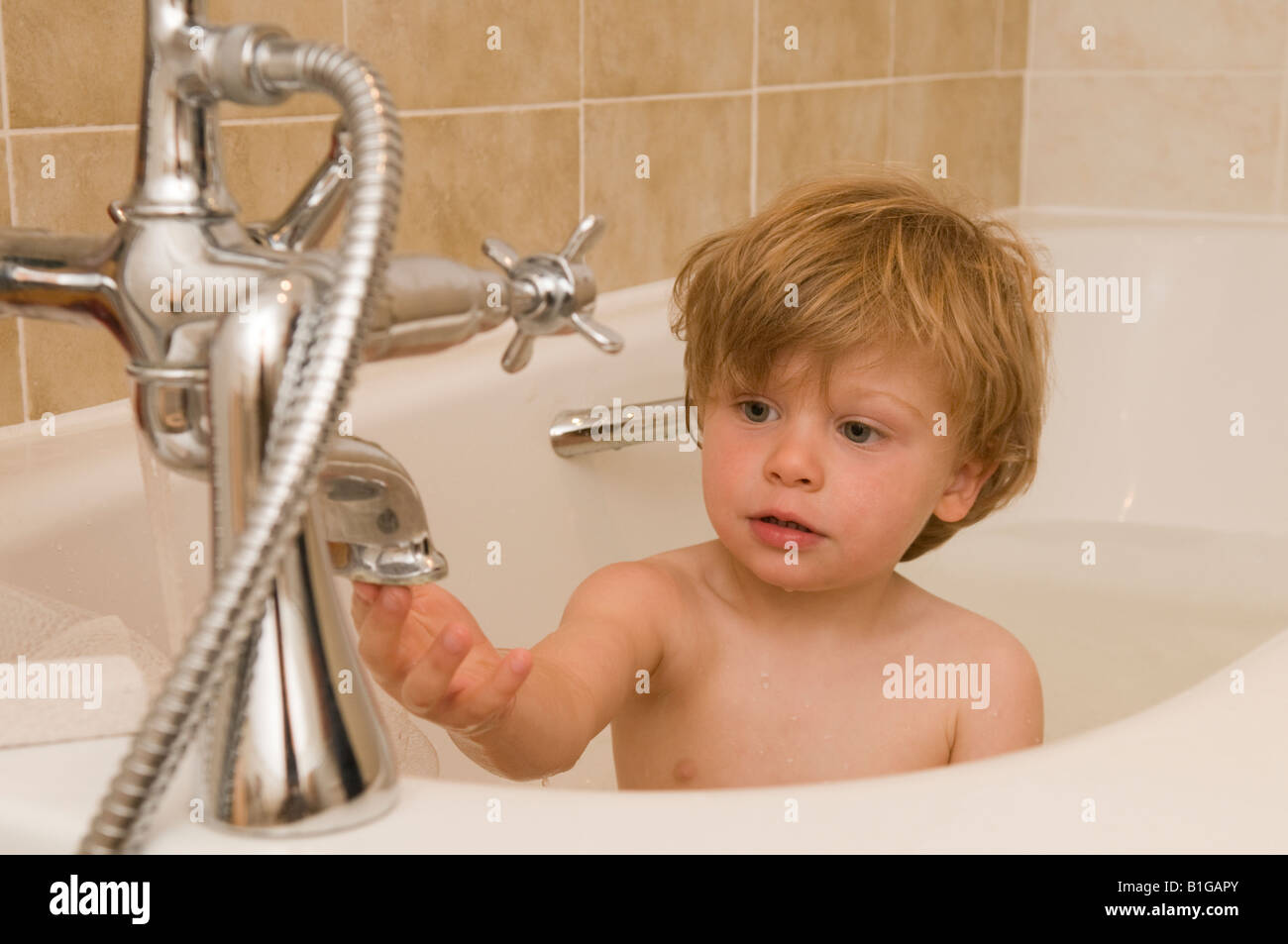Boy twentyseven months old in bath playing with water from taps Stock