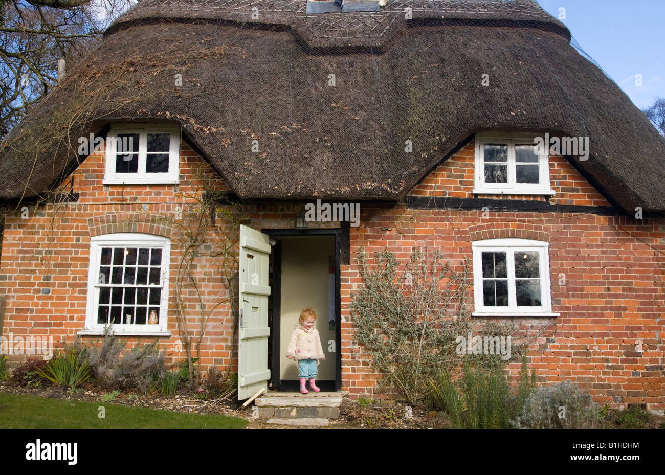 Two year old girl stepping out of the door of a thatched cottage Stock Photo