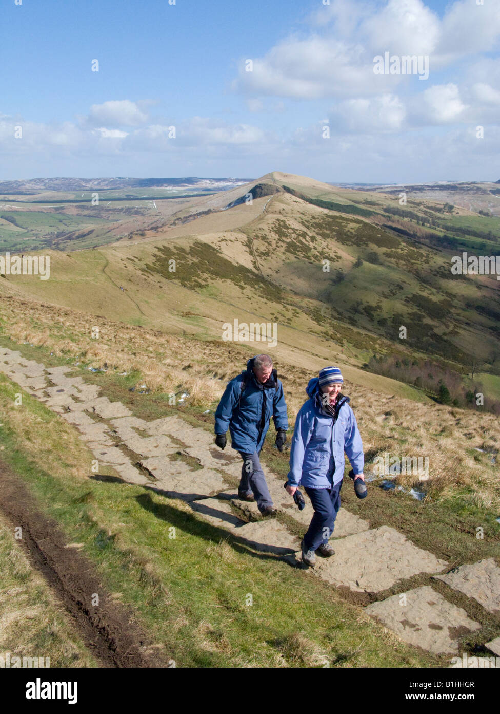 couple walking the paved footpath over Mam Tor, with a dusting of snow in the shadows. Peak District National Park. UK Stock Photo