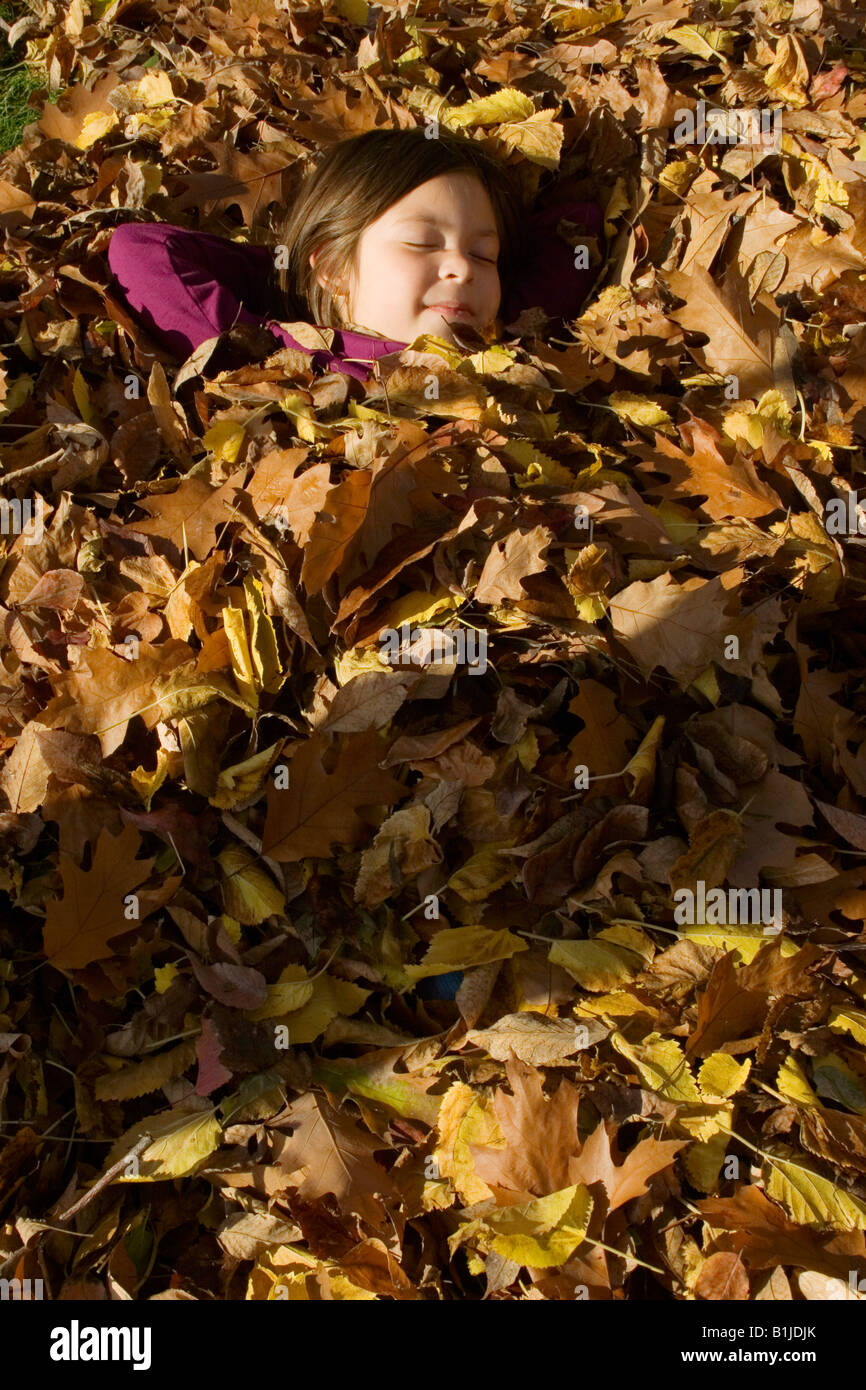 Young girl sleeps under a pile of raked oak leaves in the sunshine in Idaho during Autumn Stock Photo