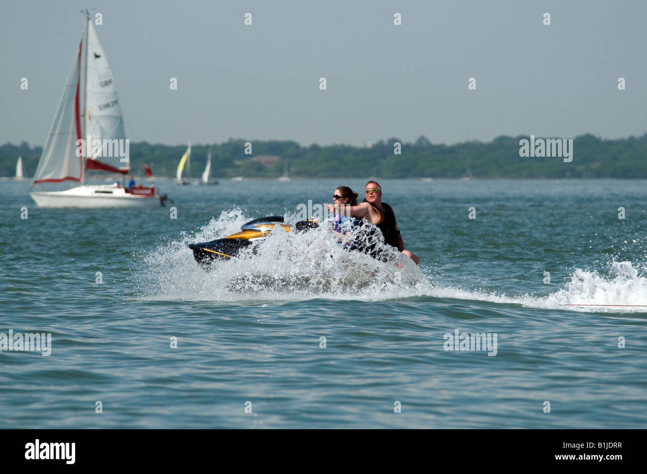 Jet bike on the sea with white waves crashing off the front being ridden by two people one facing backwards Stock Photo