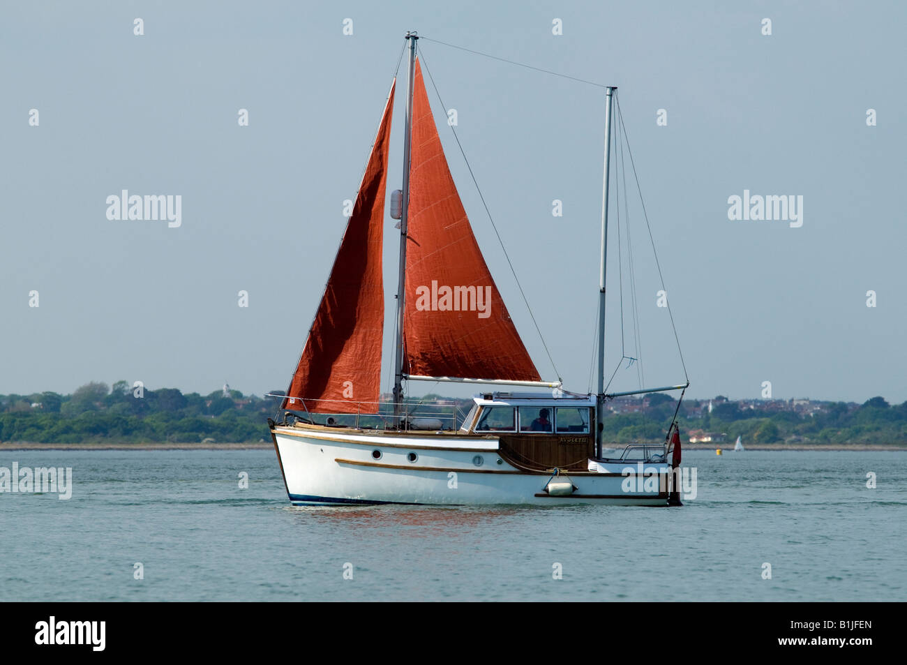 wooden cabin sailing boat with red sails side on at sea Stock Photo