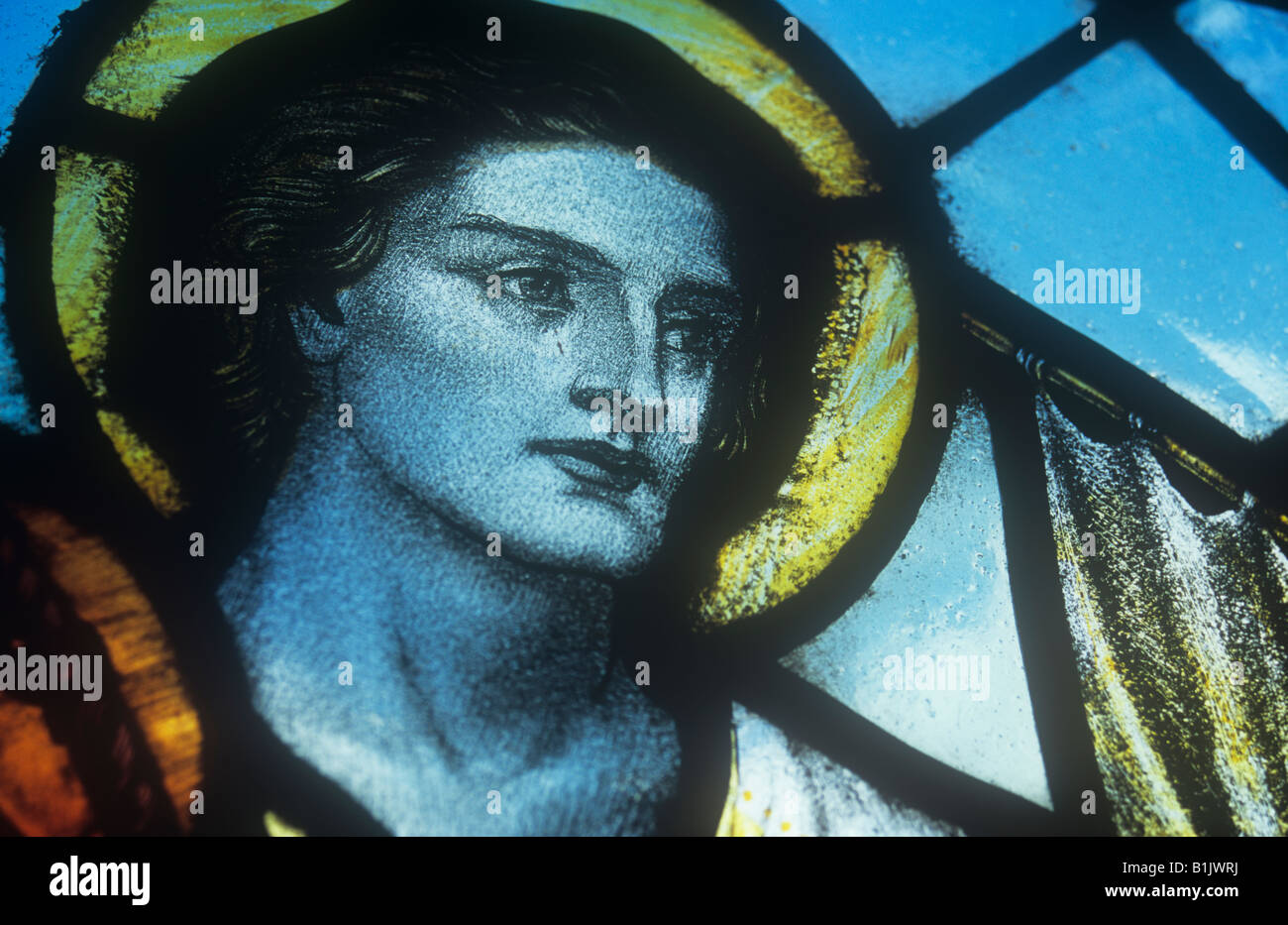 Detail of early 20th century stained glass window showing head and shoulders of St Andrew with halo and blue sky Stock Photo