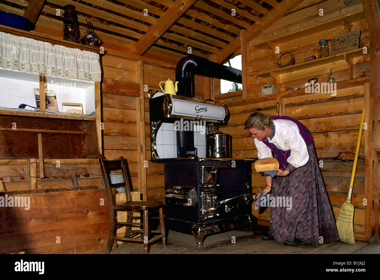Woman Re-enactor baking Bread in Old Cook Stove Oven at CottonWood House Historic Site near Quesnel, British Columbia, Canada Stock Photo
