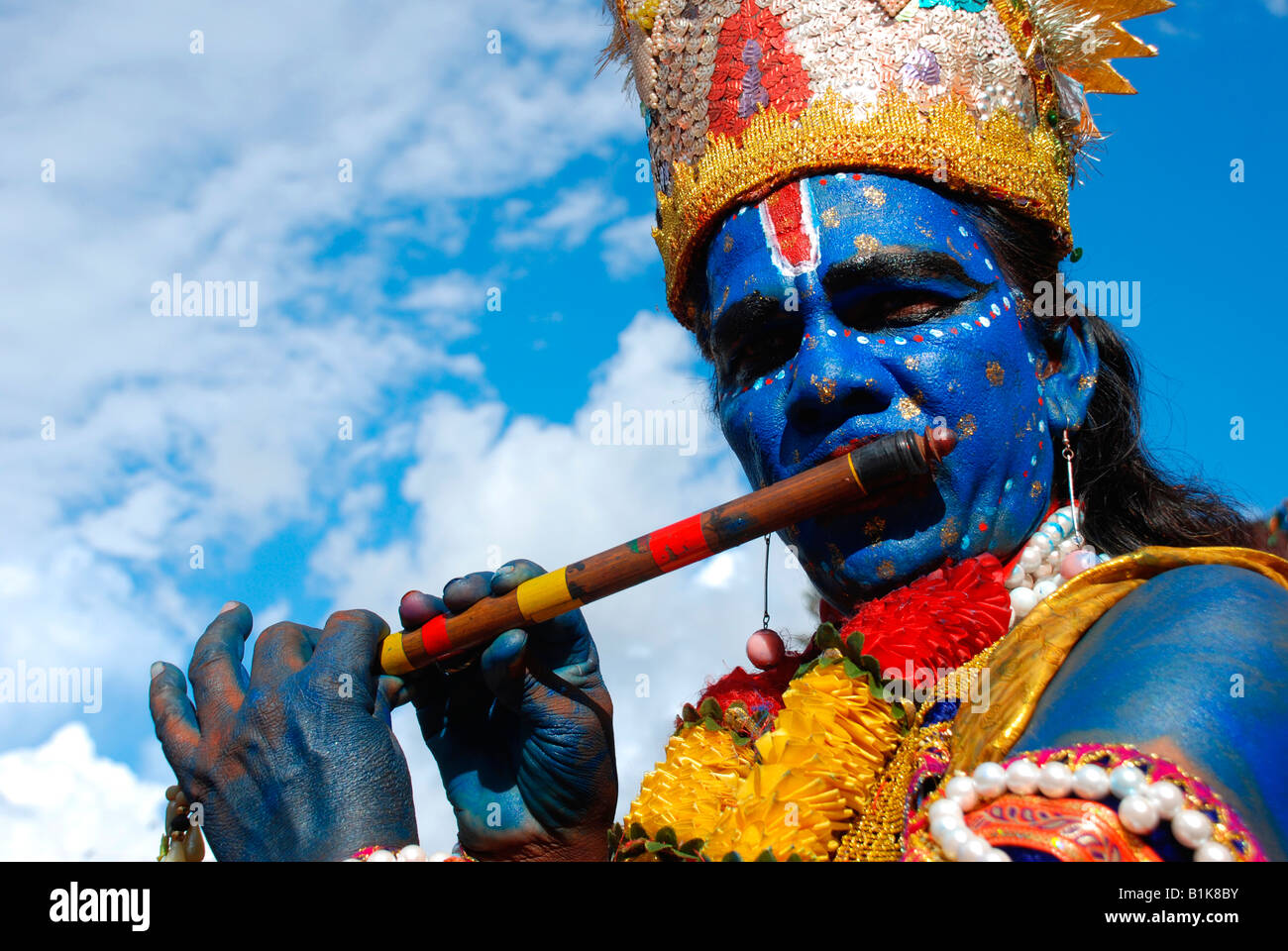 Krishna impersonator painted blue playing the flute Stock Photo