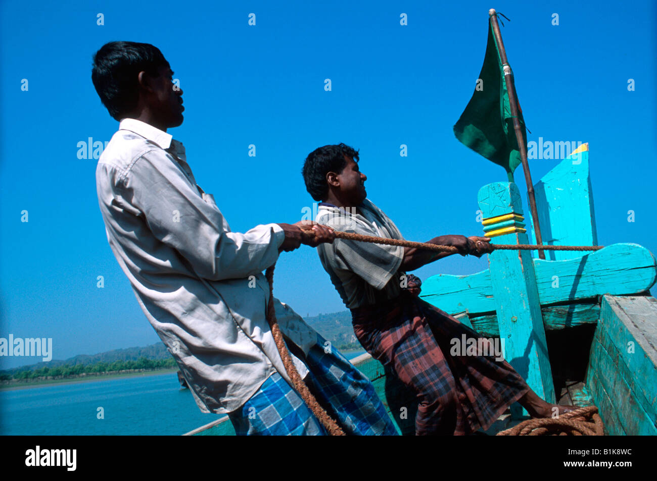 Men wearing lungis hoisting anchor near Teknaf Bangladesh Stock Photo