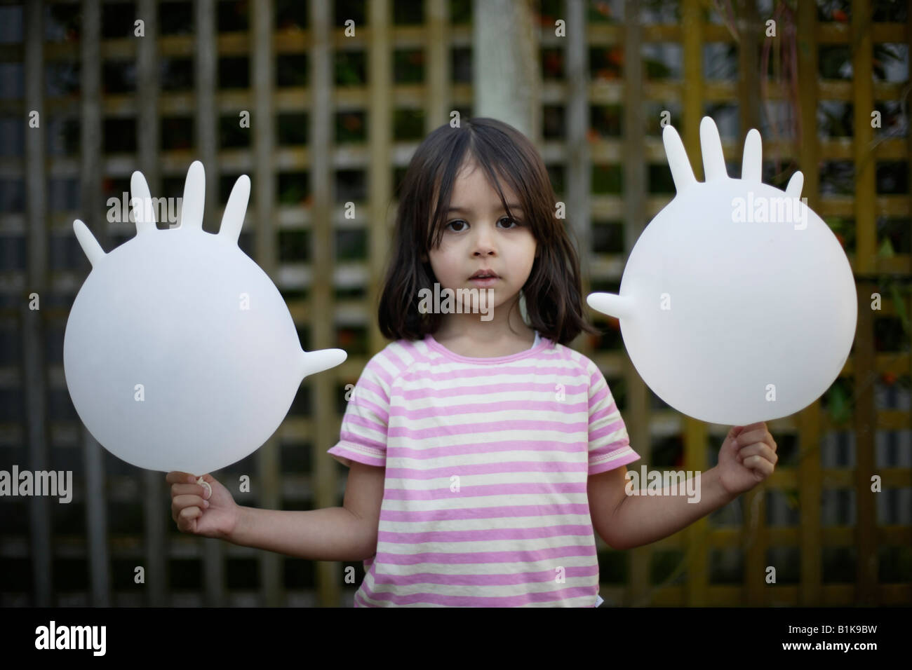Girl aged four holds two inflated latex rubber gloves and looks directly at camera Stock Photo