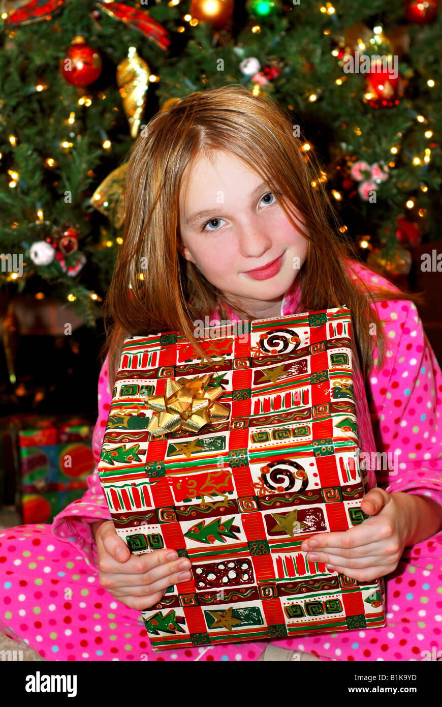 Young girl holding a big Christmas present sitting under a Christmas ...