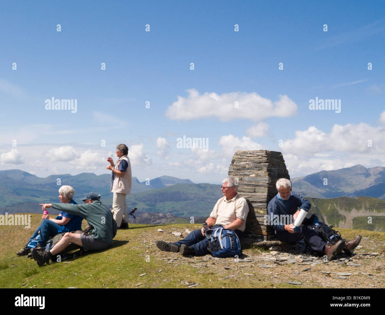 Group of Welsh Ramblers sitting by a summit cairn trig point on Moelwyn Mawr in Snowdonia National Park in summer North Wales UK Stock Photo
