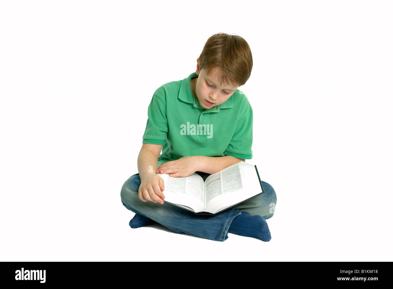 Boy of primary school age sat crossed legs reading a reference book isolated on a white background Stock Photo