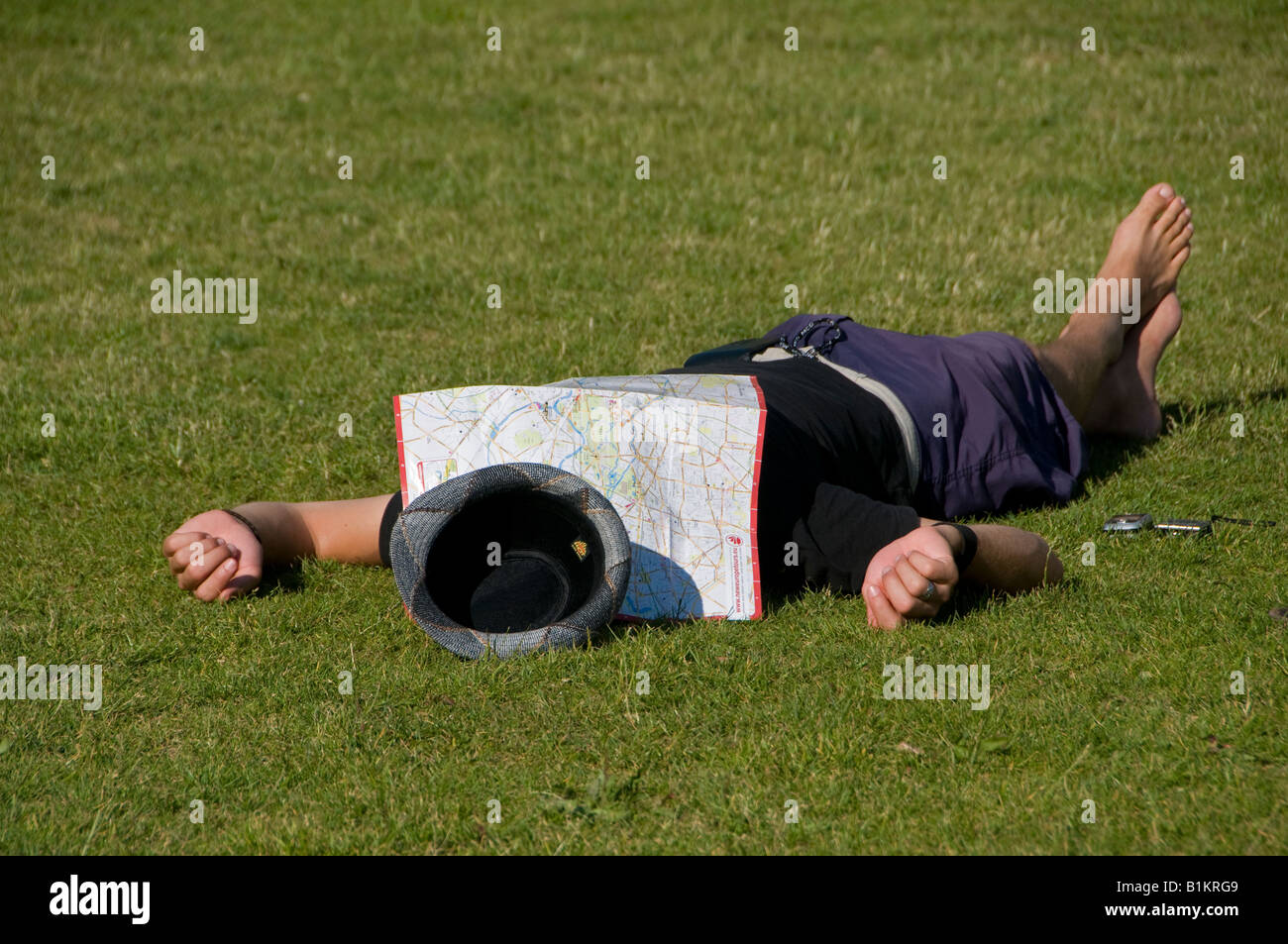 A man covers his head with a map as he takes the sun in a public park Mitte Quarter Berlin Germany Stock Photo