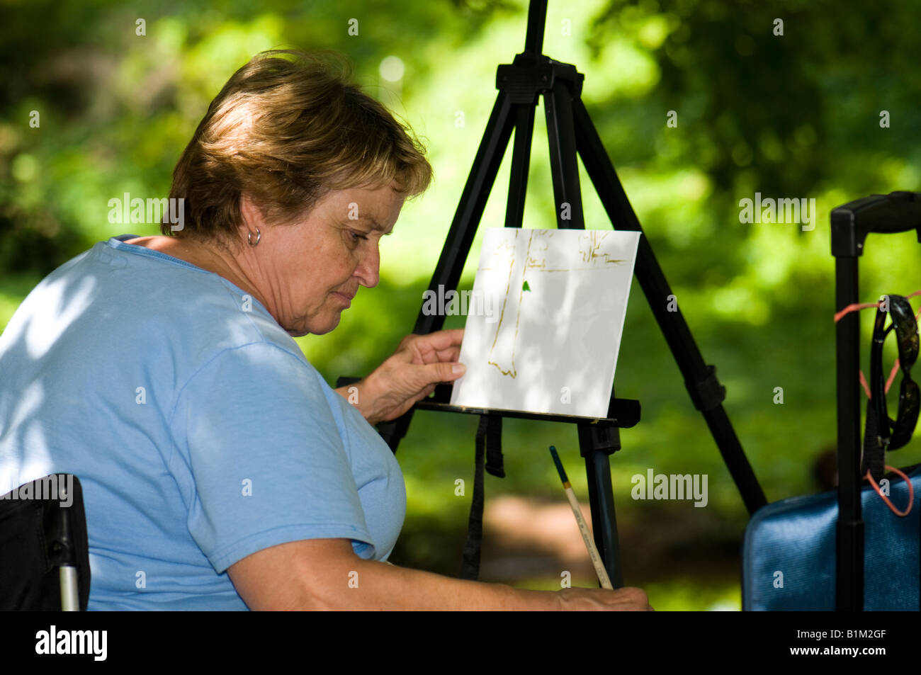 A Woman In Her 50s 60s Begins To Paint A Landscape On Location At A  a-woman-in-her-50s-60s-begins-to-paint-a-landscape-on-location-at-a