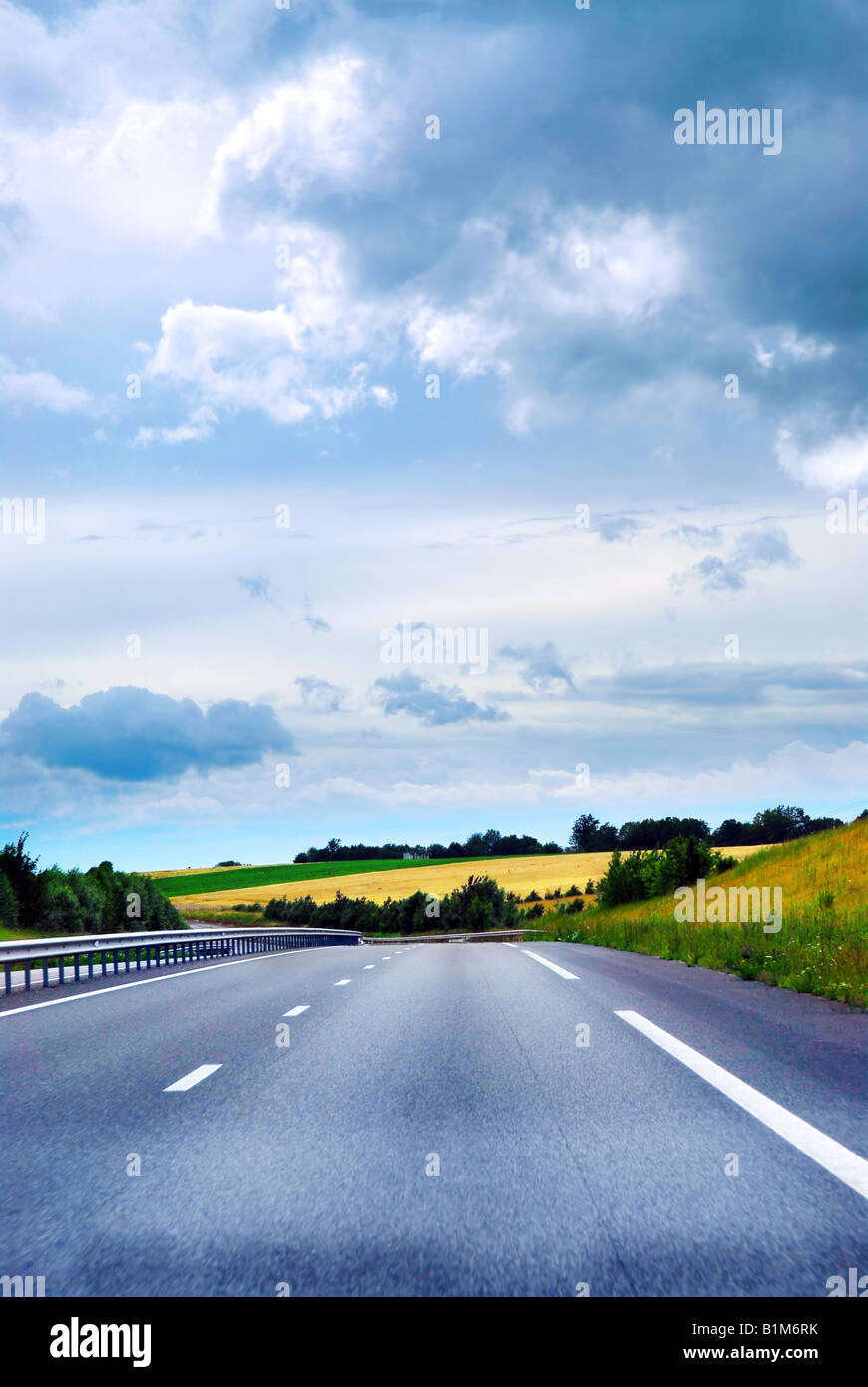 Empty road among fields with blue cloudy sky Stock Photo - Alamy