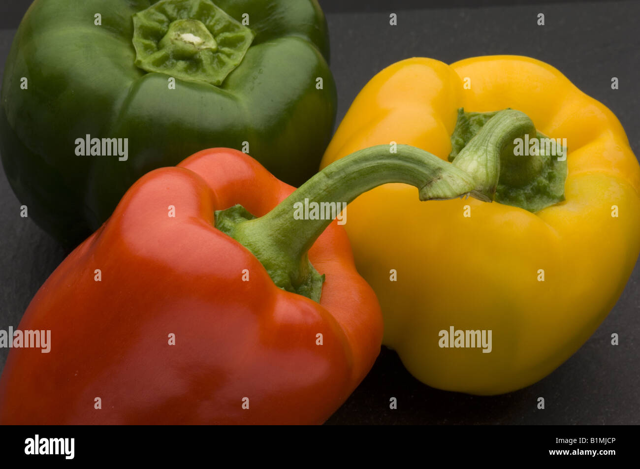 Three peppers on a black chopping board Stock Photo - Alamy
