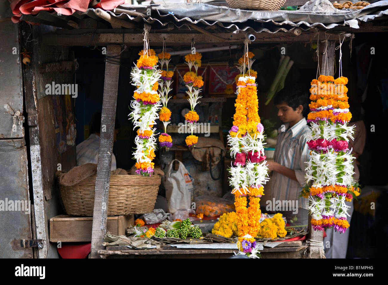 INDIA MUMBAI MAHARASHTRA Young Indian boy making and selling brightly colored garlands of flowers in a small shop Stock Photo