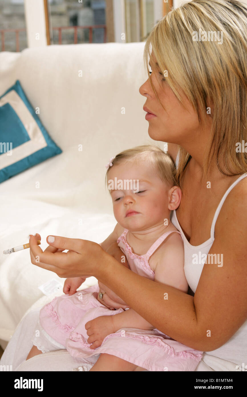 Young mother smoking with her nine month old baby sitting on her lap