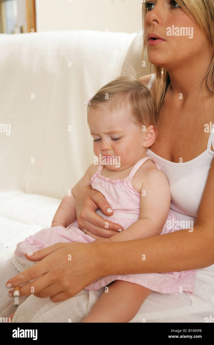 Young mother smoking with her nine month old baby sitting on her lap