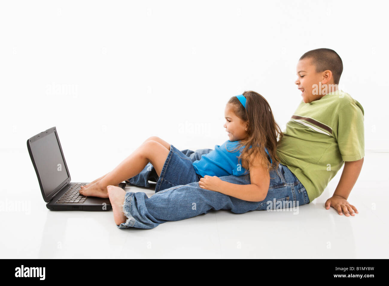 Brother and sister putting feet on laptop computer and smiling Stock