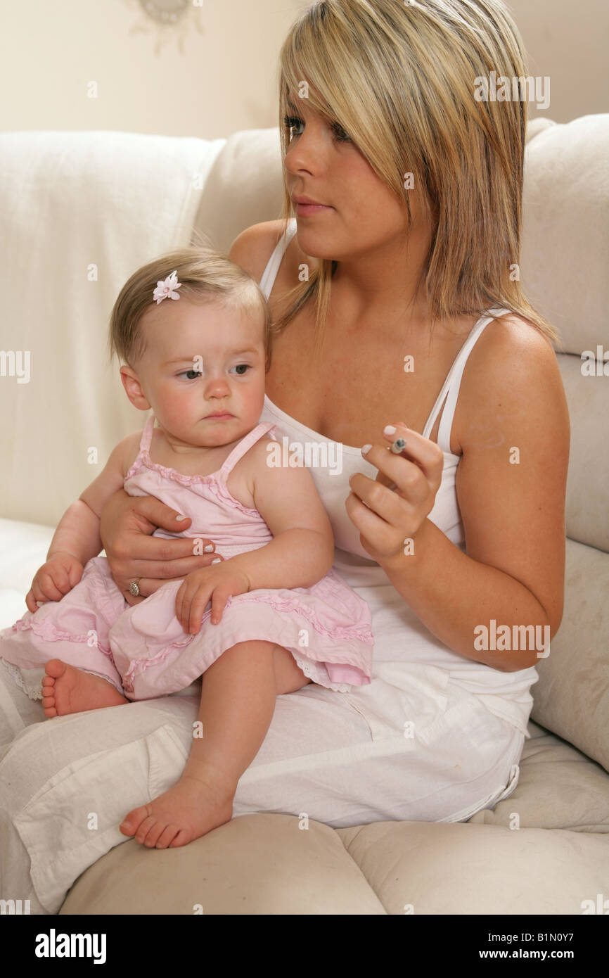 moms smoking cigarettes Young mother smoking with her nine month old baby sitting on her lap  looking at the cigarette Stock Photo