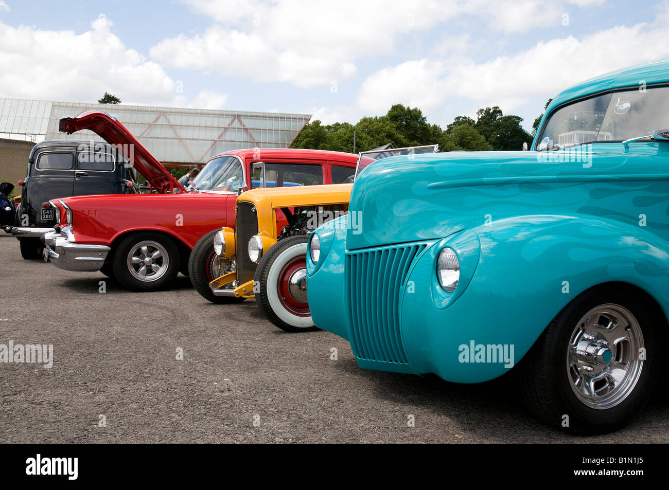 looking across the fronts of a row of parked custom cars at a rally in ...