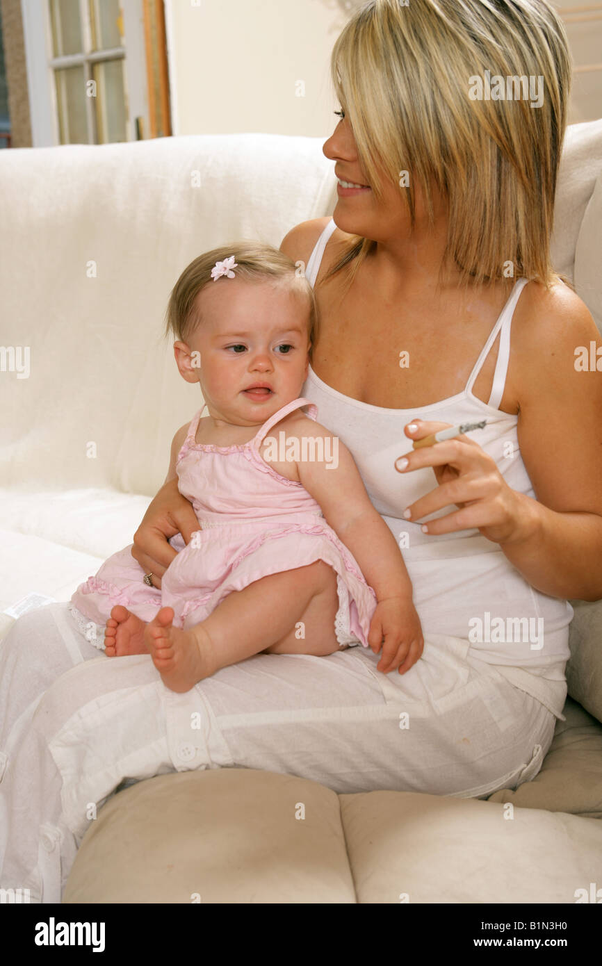 Young mother smoking with her nine month old baby sitting on her lap