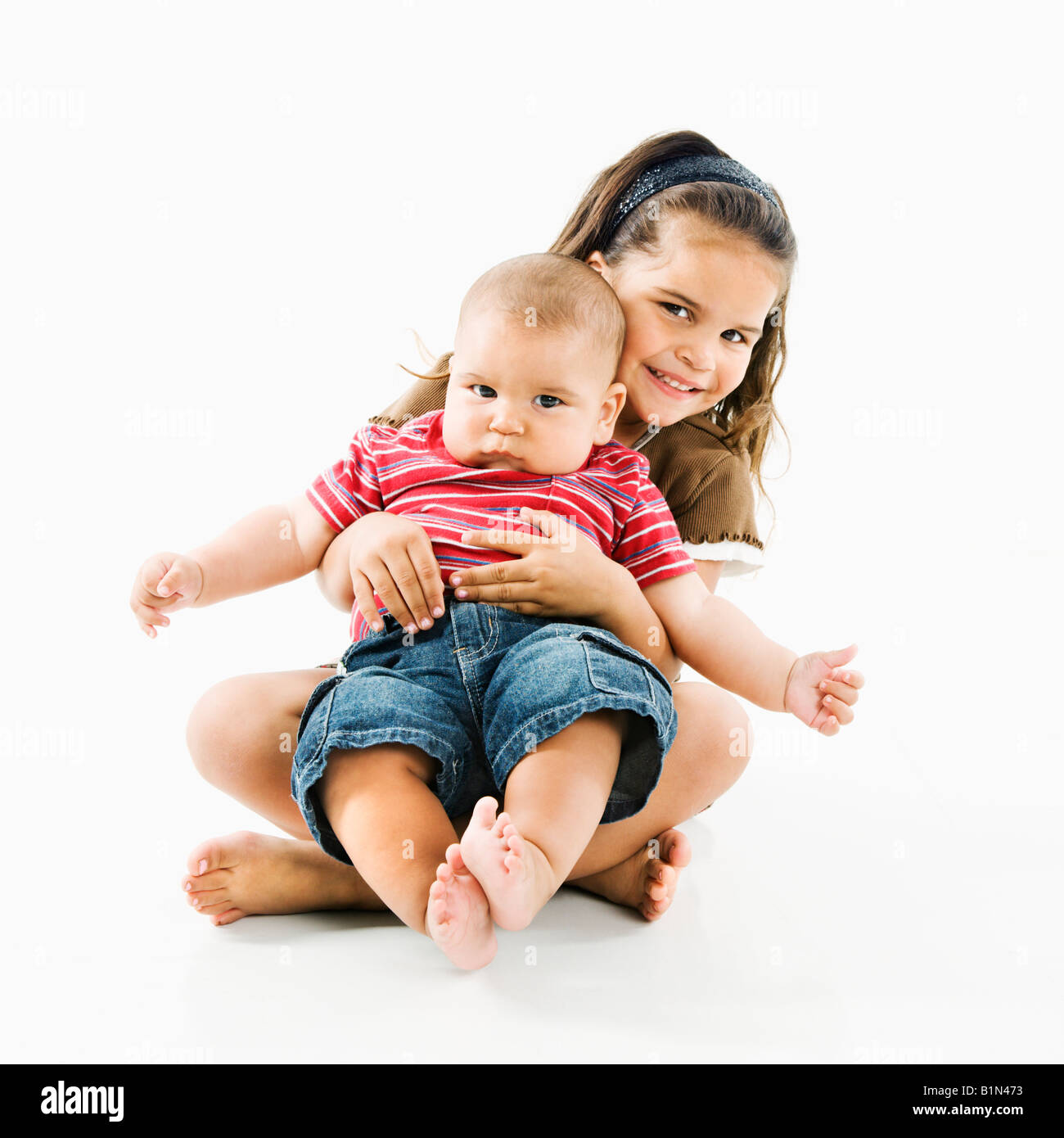 Cute little hispanic girl holding baby brother in her lap Stock Photo
