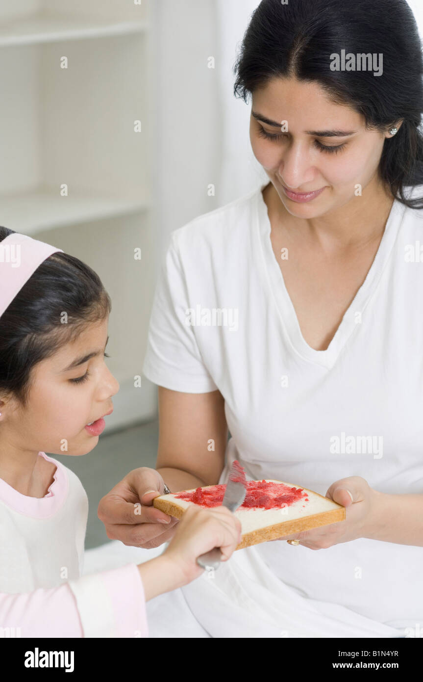 Close-up of a girl spreading jam on a bread with her mother Stock Photo