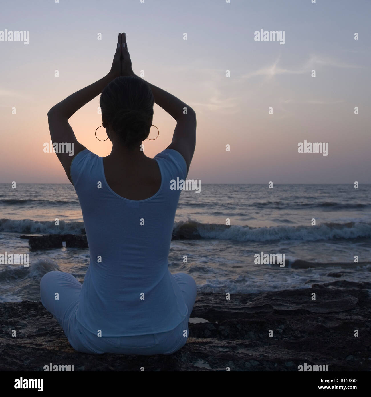 Rear view of a young woman meditating in a prayer position on the beach ...