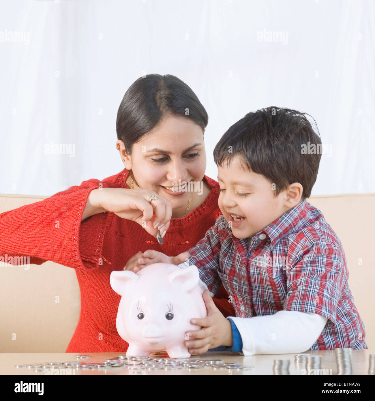 Young woman putting a coin in a piggy bank with her son sitting beside ...