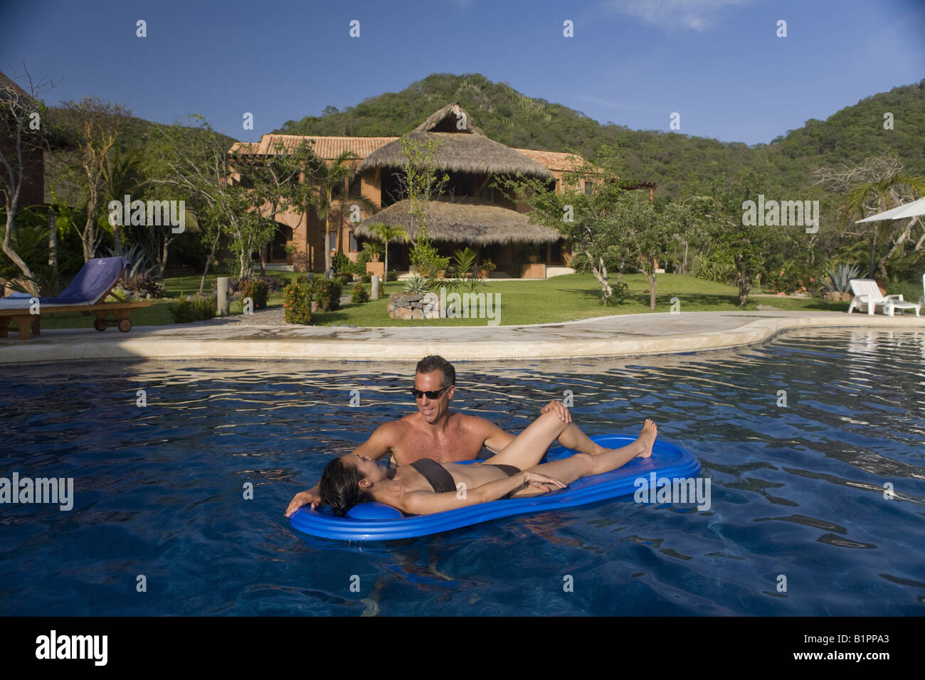 Romantic couple share a moment together in a luxurious seaside pool and villa. Stock Photo