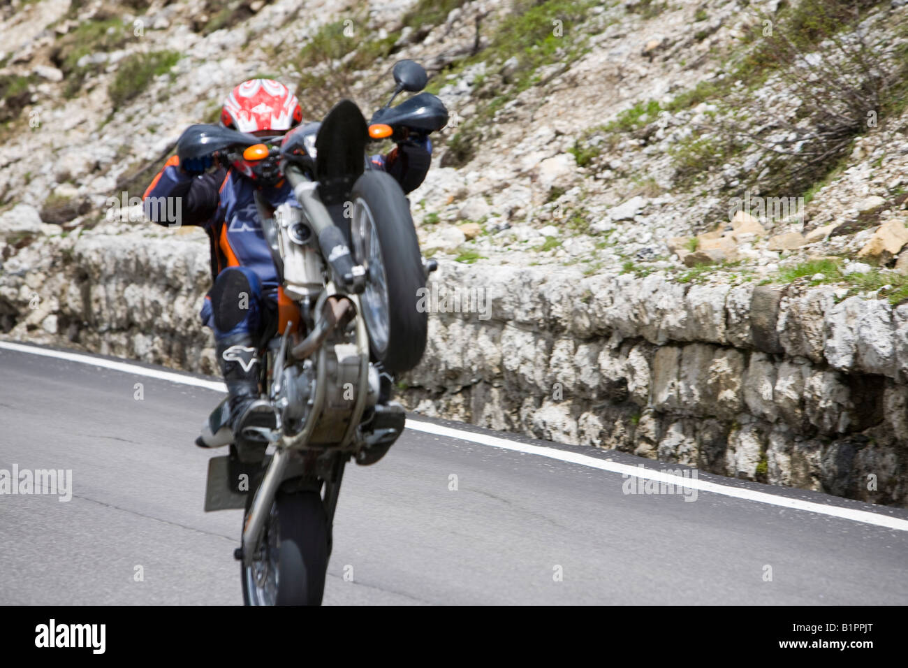 A motorbike rider showing off pulling a wheely in the Italian Dolomites on a mountain road Stock Photo