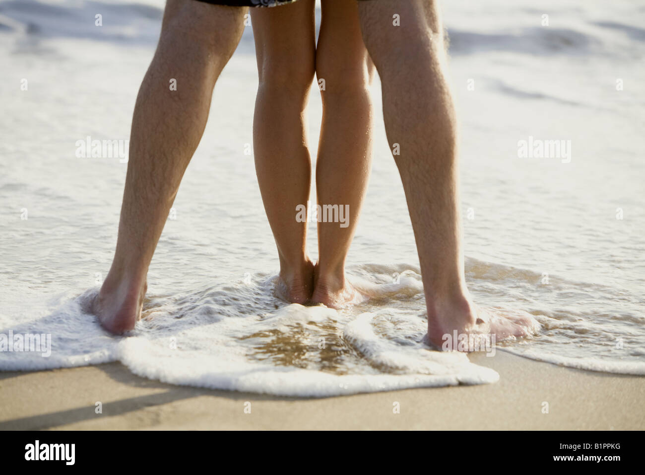 Close up of a couple's legs as they embrace and enjoy the beach and surf during a beach holiday. Stock Photo