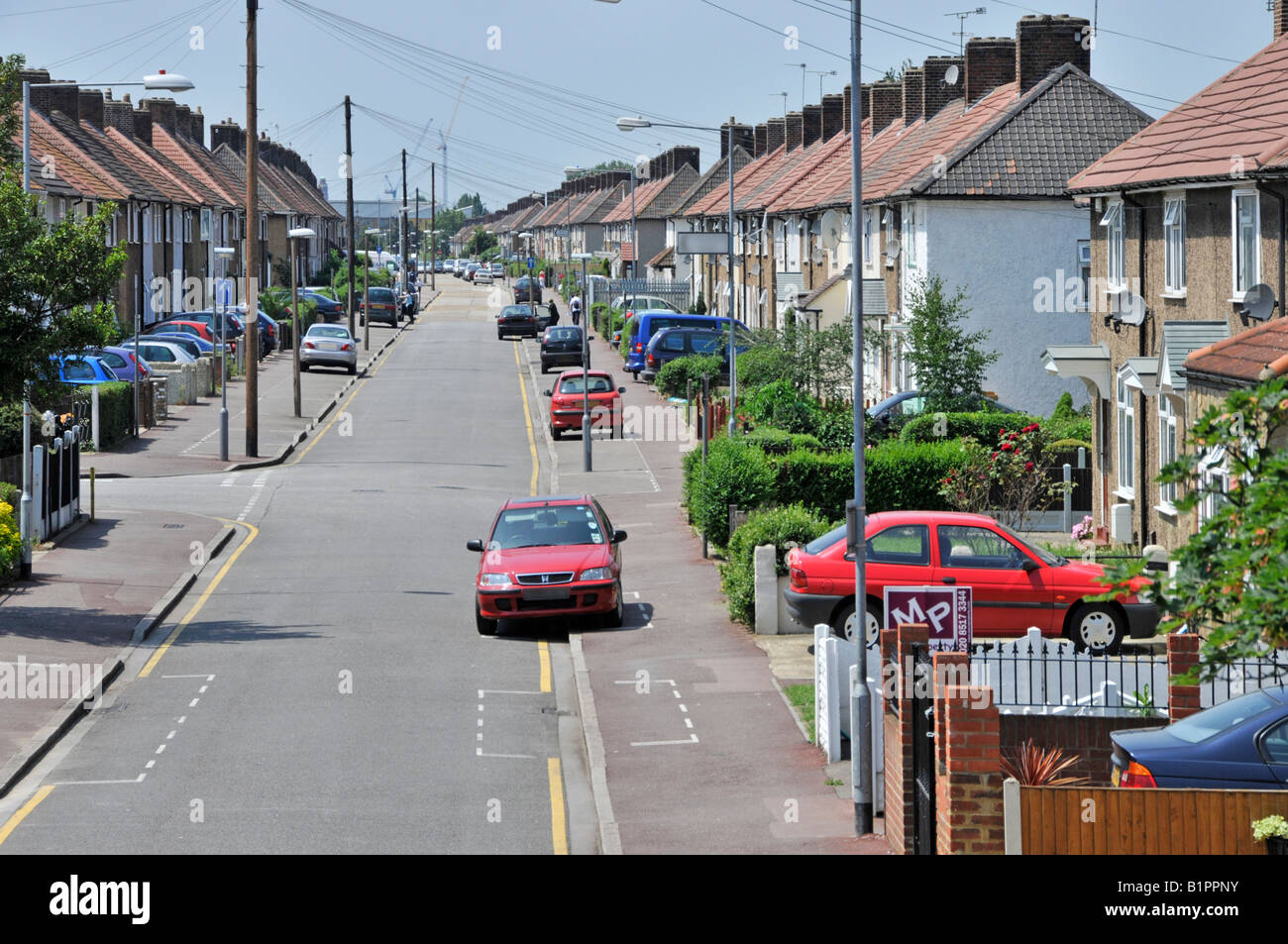 Looking down along street of cars & houses on Becontree housing estate built between the wars as social council housing homes Barking and Dagenham UK Stock Photo
