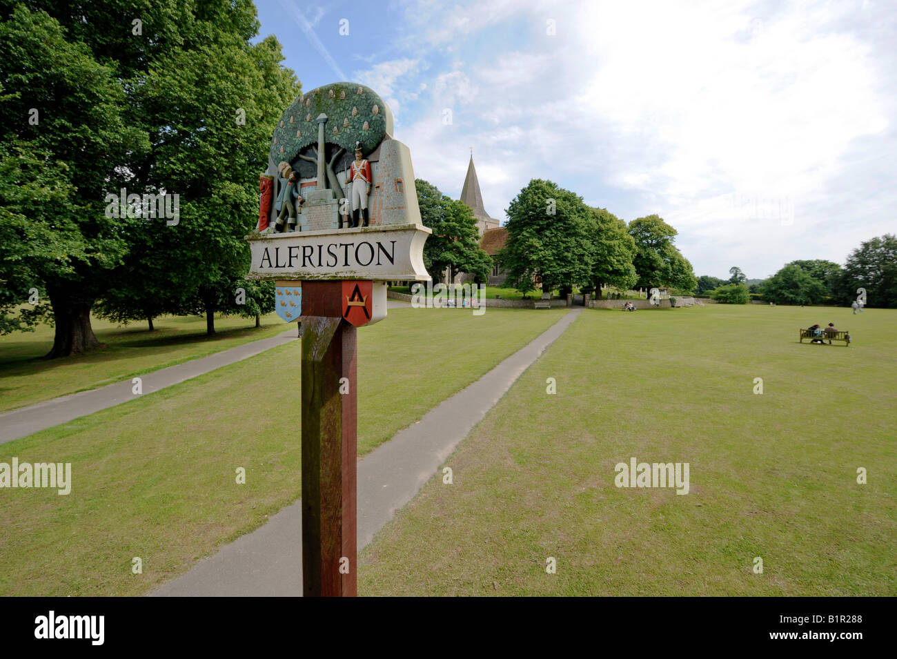 The village sign on Alfriston village green (known locally as The Tye) with St Andrews Church in background. East Sussex, UK. Stock Photo