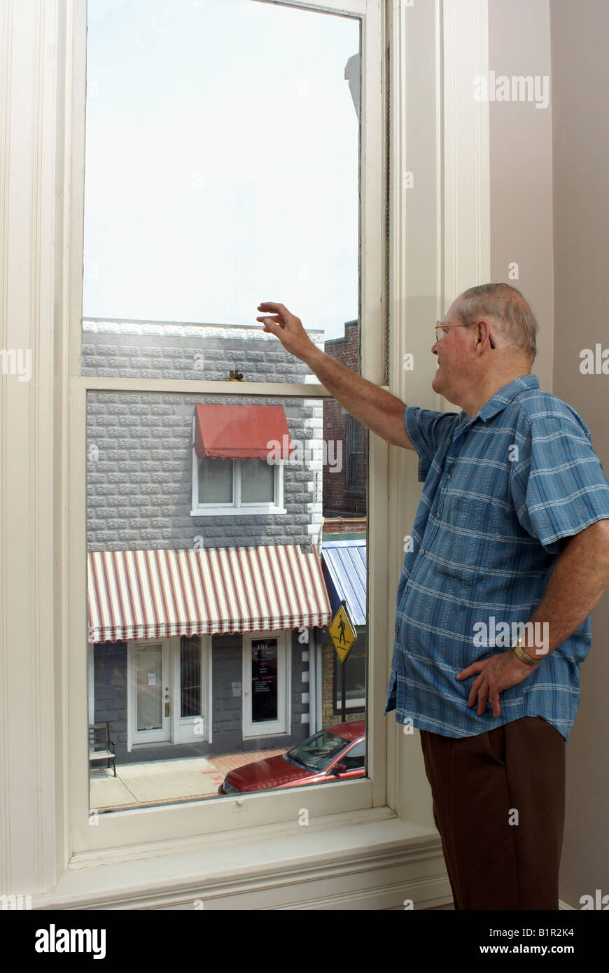 This elderly man waves at someone outside his window Stock Photo