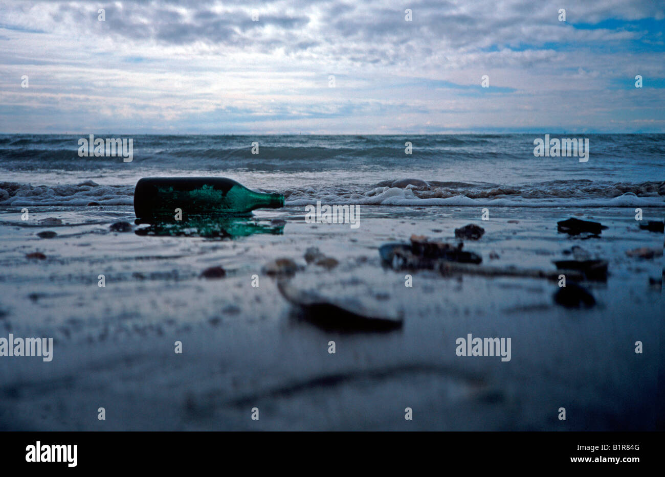 bottle and other debris abandoned on beach polluting the environment waves in the distance Stock Photo