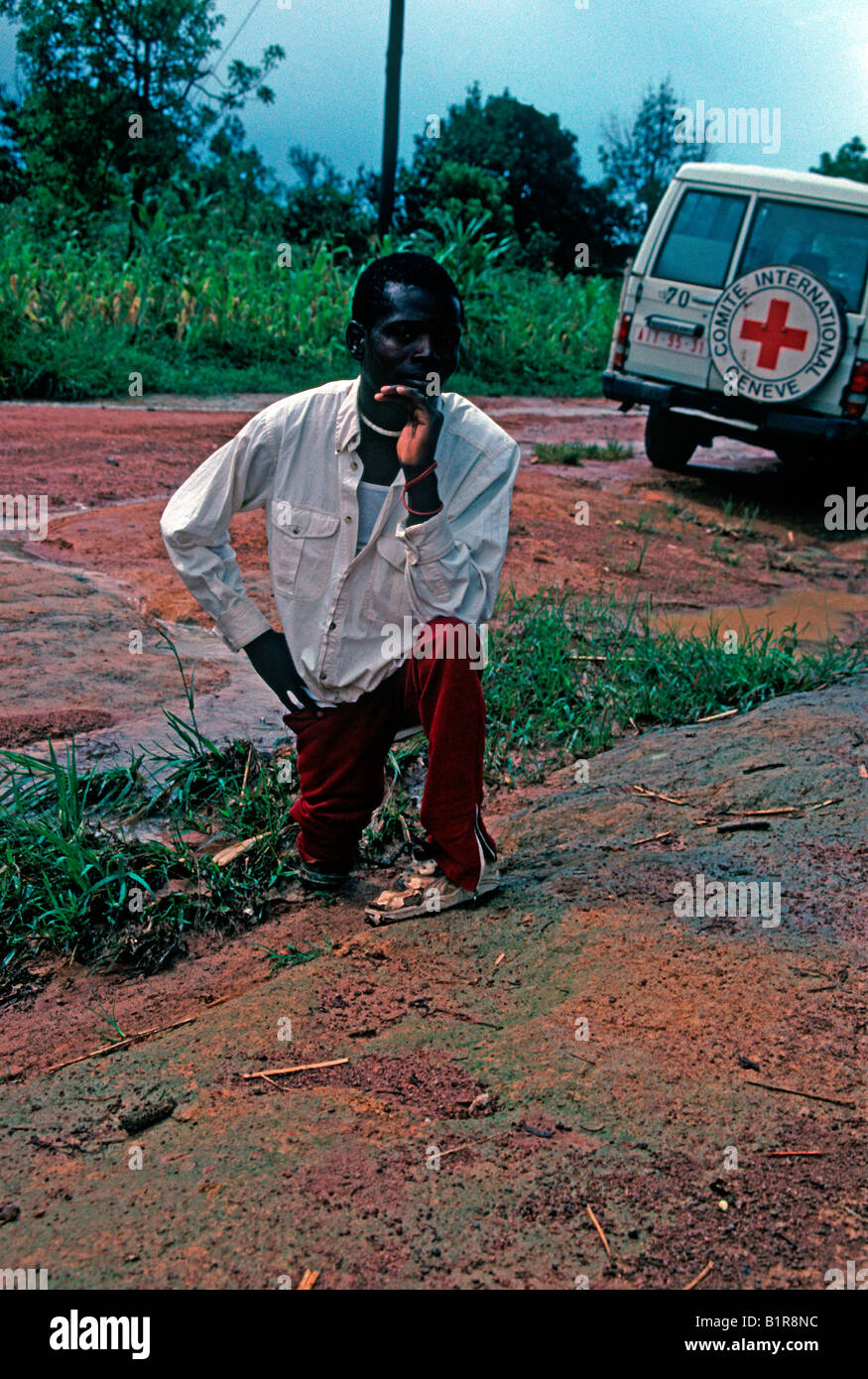 african man war veteran amputee awaiting on muddy road near red cross jeep Stock Photo