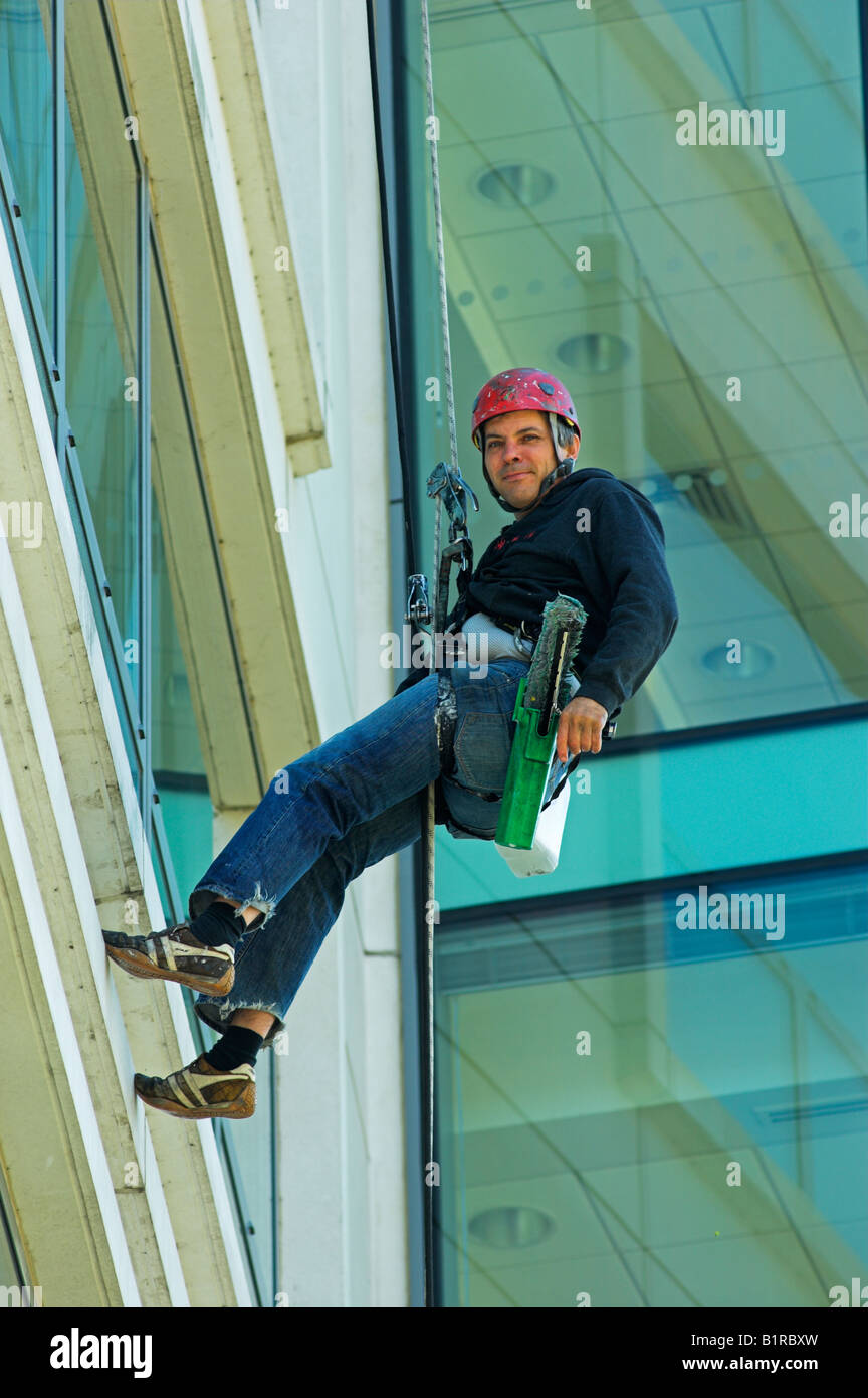 Window cleaner suspended on tall office building cleaning windows Stock Photo