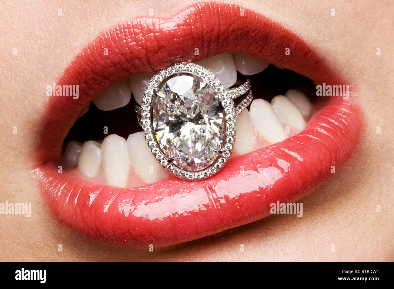 A womans mouth holding a giant diamond ring with her teeth Stock Photo