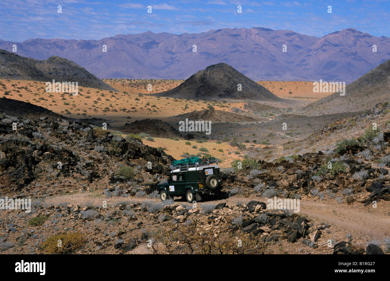 Land Rover in stony desert landscape, Brandberg Mountain backdrop, near Uis, Namibia, Africa Stock Photo