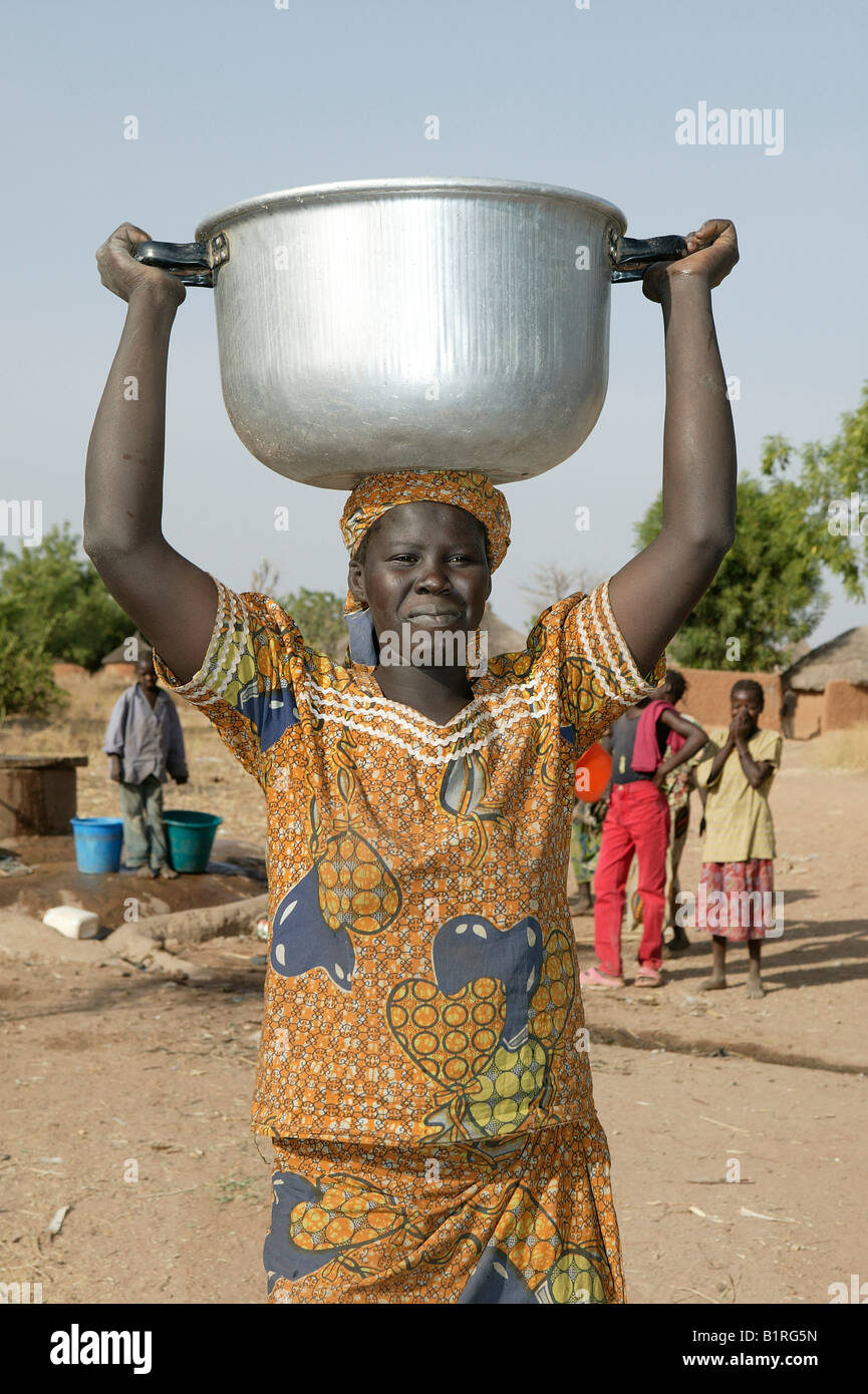 Woman carrying a pot of water on her head, well behind her, Pakete, Cameroon, Africa Stock Photo