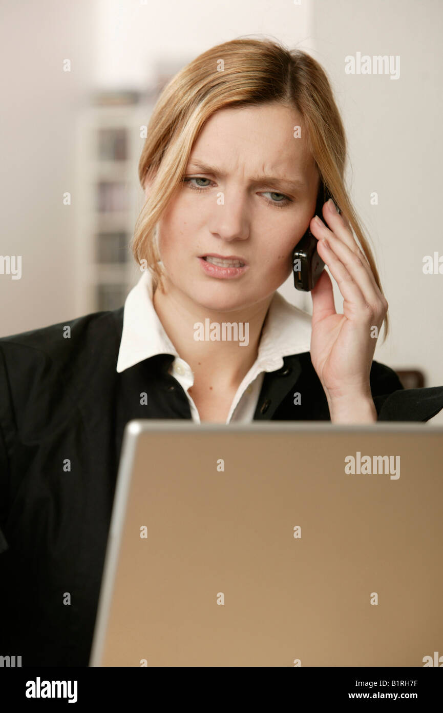 Blonde woman getting annoyed on the telephone at a laptop Stock Photo