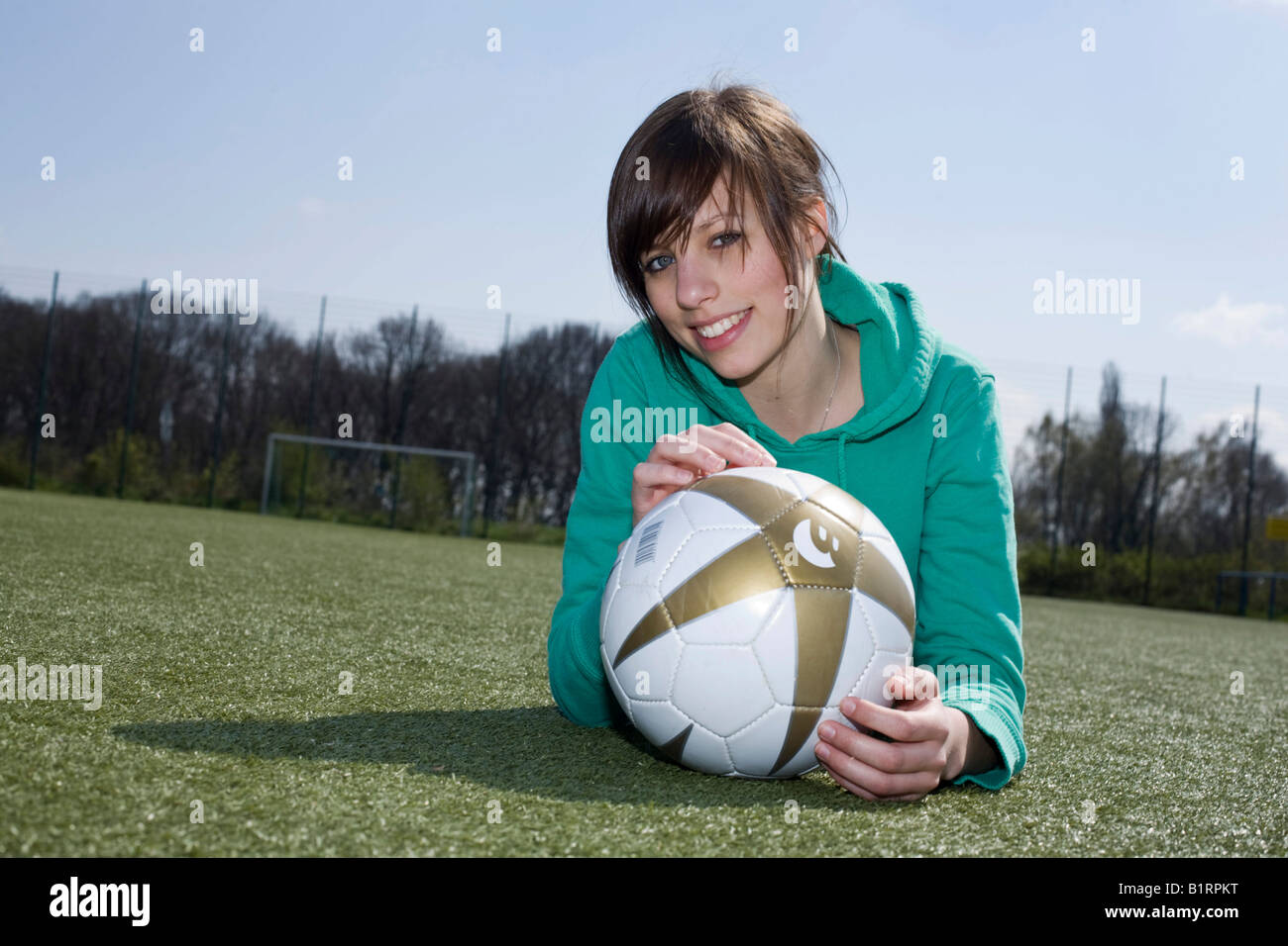 Young woman lying with a football in front of her on a football pitch Stock Photo
